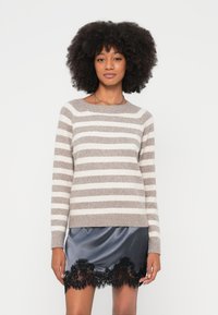 Dryžuotas megztinis smėlio ir kremine spalvomis, suapvalinta iškirpte ir ilgomis rankovėmis, derinamas su juoda satino sijonu su nėrinių apdaila.