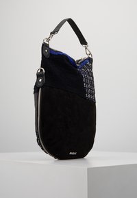 Czarna zamszowa torba na ramię z fakturowanymi panelami, srebrnym zamkiem błyskawicznym oraz tkaninowym akcentem w niebieskie i kratkowane wzory. Okrągły kształt.