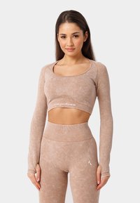 Beige crop top met lange mouwen, zachte textuur, ronde halslijn en subtiele branding. Gecombineerd met hoge taille leggings van dezelfde stof.