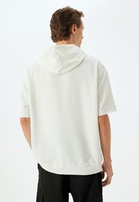 Lichtgrijze hoodie met korte mouwen en een ruime capuchon, gemaakt van zacht materiaal. Heeft ribbelboorden aan de onderkant en bij de mouwen; minimalistisch ontwerp zonder graphics.
