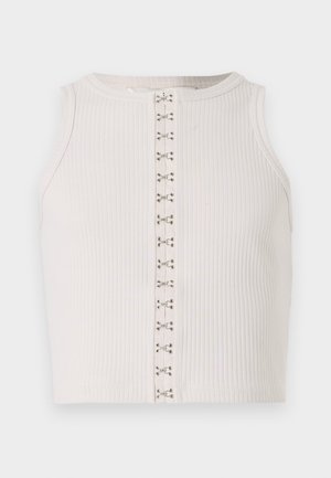 Top corto a coste bianco con collo alto, dotato di una chiusura frontale decorata con piccoli fermagli in metallo argentato. Texture liscia.