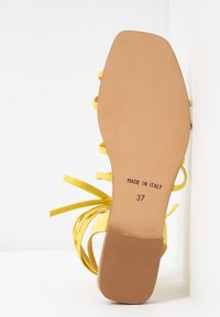 Semelle d'une sandale jaune à brides indiquant la taille 37 et le texte "Made in Italy" sur un fond clair.