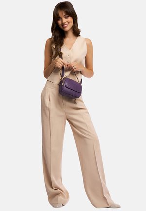 Pantaloni beige a righe sottili e una canotta, che tiene una piccola borsa viola texturizzata con una tracolla in oro. Scarpe lisce e lucide.