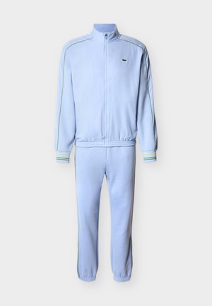 Veste de survêtement bleu clair à fermeture éclair complète et pantalon assorti avec piping vert et petit logo brodé sur la poitrine gauche.