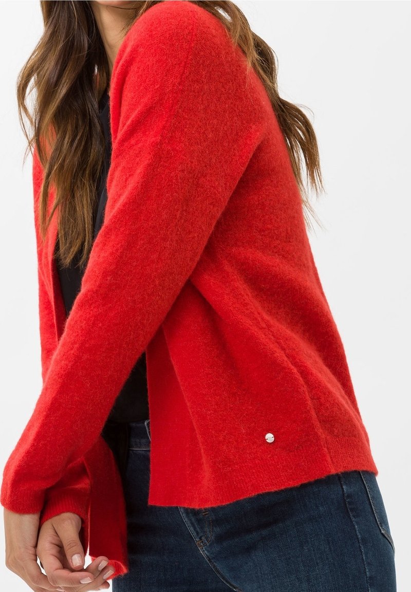 Czerwona, puszysta kamizelka z luźnym krojem, długimi rękawami i srebrnym akcentem na dole. Nosi się ją na czarną bluzkę i ciemne dżinsy.