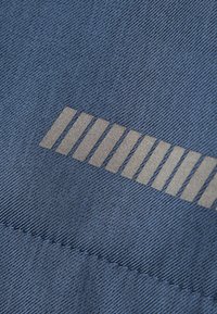 Tessuto denim di colore blu scuro con una texture liscia, caratterizzato da una serie di strisce rettangolari e quadrate di colore grigio chiaro vicino al bordo.