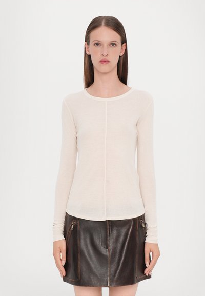 Haut à manches longues, couleur blanc cassé, avec un col rond et une texture légère et transparente, associé à une jupe en cuir marron foncé avec des détails zippés.