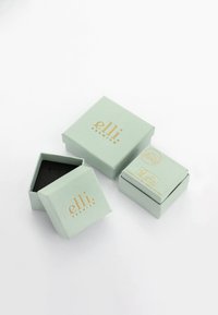 Mintgrønne papirsmåneder med mat finish, der har guldfoil-tekst. Én æske er åben og afslører et sort indre.