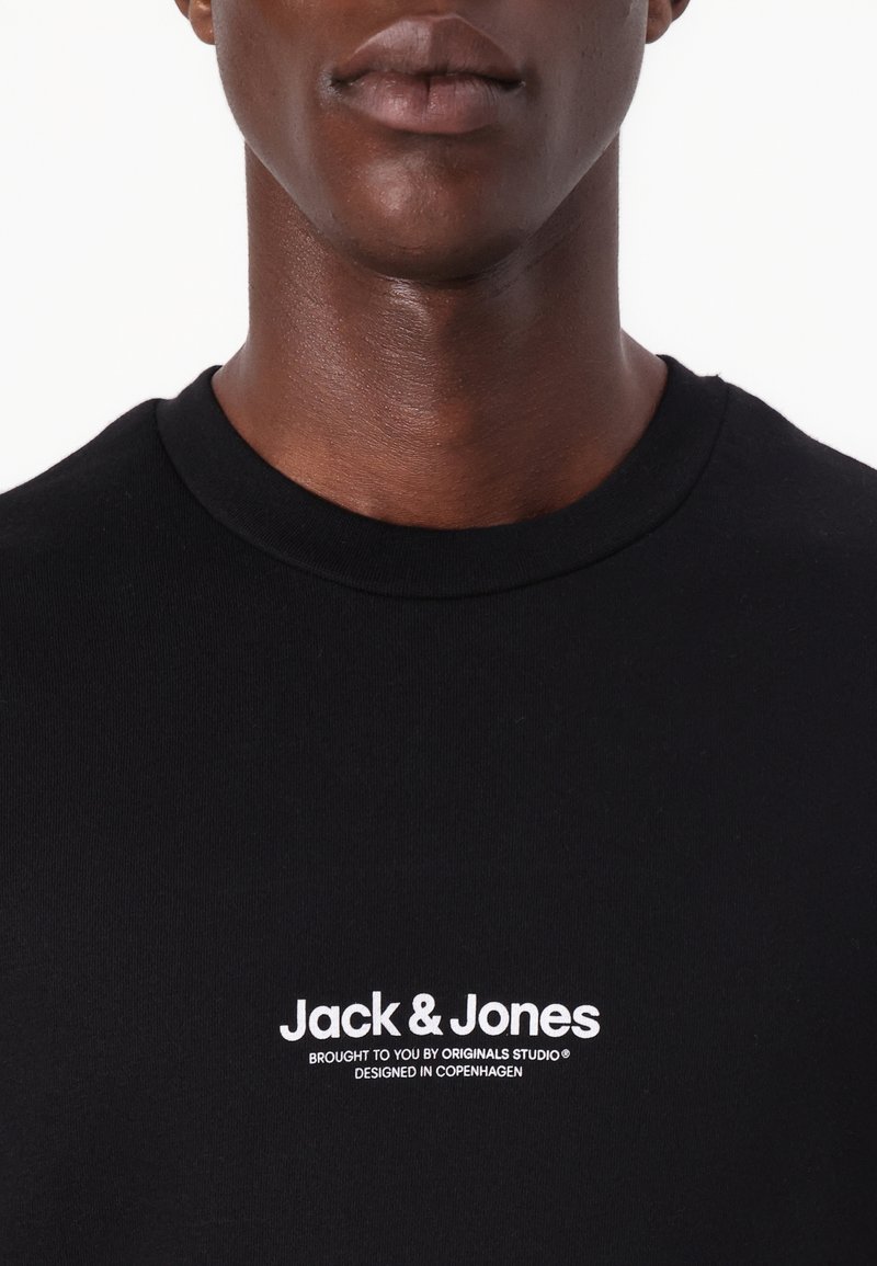 Schwarzes Baumwoll-T-Shirt mit rundem Halsausschnitt und weißem Textlogo "Jack & Jones" mit zusätzlichem Text darunter, der eine glatte Textur zeigt.