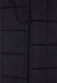 Tissu noir matelassé avec des coutures carrées et un petit curseur de fermeture éclair noir centré verticalement.