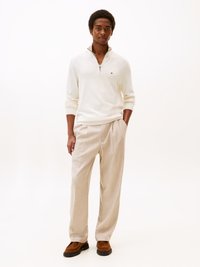 Maglione bianco con zip, pantaloni beige a vita alta e scarpe marroni. L'outfit presenta una vestibilità rilassata e una texture morbida.