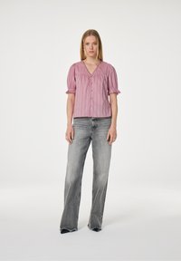 Roze blouse met korte mouwen en een V-hals, knoopsluiting aan de voorkant en textuurdetails, gecombineerd met grijze flare jeans met een raw hem.
