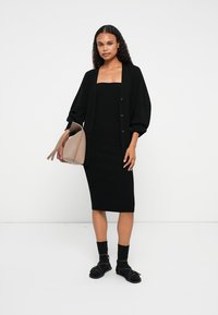 Μαύρο ριγωτό midi φόρεμα με τετράγωνη λαιμόκοψη, καλυμμένο με μια μαύρη υπερμεγέθη ζακέτα. Συμπληρώθηκε με μια μπεζ τσάντα και μαύρες σάντες.