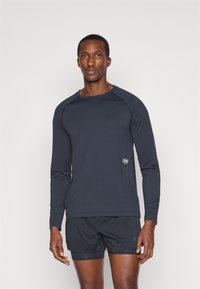 Camisola desportiva de manga longa em azul marinho escuro, feita de um tecido leve. Apresenta um decote redondo e um logotipo discreto na parte inferior da frente.