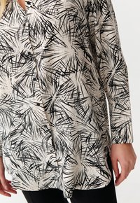 Blusa con stampa di foglie di palma in bianco e nero con una vestibilità lunga e morbida, dotata di bottoni, realizzata in tessuto morbido con una texture liscia.
