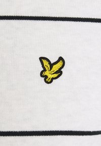Tessuto bianco con strisce nere, caratterizzato da un logo di un uccello giallo ricamato sul petto. Il materiale presenta una texture a maglia fine.