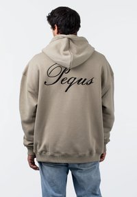Beige oversize kapucnis pulóver, húzózsinórral. Fekete, dőlt betűs "Pequs" felirat a hátrészén, bordázott mandzsetták és hem. Látható varrási textúra.