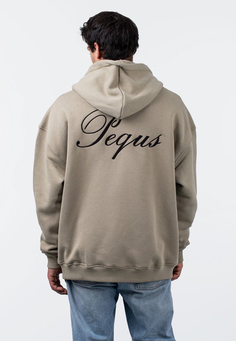 Beige oversize kapucnis pulóver, húzózsinórral. Fekete, dőlt betűs "Pequs" felirat a hátrészén, bordázott mandzsetták és hem. Látható varrási textúra.