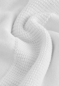 Tessuto bianco testurizzato disposto in pieghe, caratterizzato da una miscela di modelli a maglia, con una superficie morbida e pelosa e una finitura liscia e lucida.