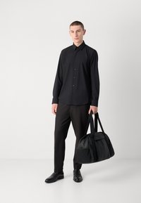 Svart skjorte med lange ermer, kombinert med svarte bukser og en teksturert svart duffelbag. Glatt stoff og minimal design.
