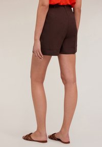 Shorts marroni a vita alta con una texture liscia, orlo piegato e tasche laterali, abbinati a sandali marroni con cinturini.