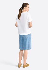 Top alb cu mânecă scurtă, croială lejeră. Purtați cu pantaloni scurți din denim albastru deschis și încălțăminte bej. Design simplu, fără modele sau logo-uri vizibile.