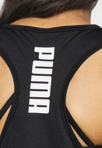 Czarny sportowy top na ramiączkach z teksturowanej tkaniny, z dużym białym logo "PUMA" na plecach i krzyżującym się wzorem ramiączek.