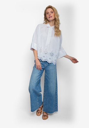 Witte katoenen top met een kraag en korte mouwen, voorzien van een ingewikkeld bloemrijk borduursel bij de zoom. Gecombineerd met wijde blauwe denim jeans.