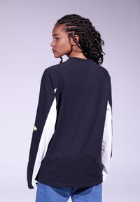 Long-sleeve shirt with a black body, white sleeves, and gold accents. Features a crew neck and a relaxed fit. Soft cotton material.