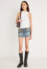 Λευκό ριμπ αμάνικο τοπ, μπλε μίνι φούστα τζιν με χρυσούς κυκλικούς τρουκς και σχέδια, μαύρες μπότες μέχρι το γόνατο και μικρή καφέ τσάντα χειρός.