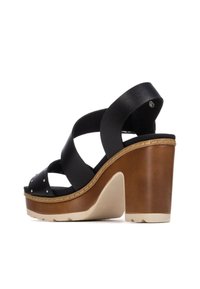Sandalia cuña de cuero negro con tiras cruzadas, plataforma de madera, detalles de tachuelas y tacón marrón claro. Suela texturizada para mayor tracción.