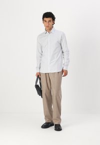 Gestreiftes Hemd in Hellblau und Weiß, kombiniert mit beigen Hosen. Eine schwarze Tasche und Schuhe vervollständigen das Outfit. Minimalistisches Design.
