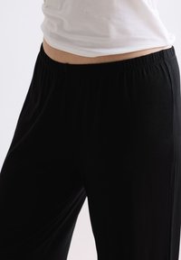 Zwarte, losse broek met een elastische tailleband. Gemaakt van zachte stof, met een gladde textuur en een rechte pijp.