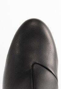 Zapato de cuero negro con punta redonda y textura suave. Costura notable en la parte delantera, que ofrece un diseño elegante.