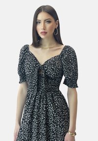 Robe noire à fleurs avec des manches bouffantes, un détail en trou de serrure et une taille smockée. Caractéristiques de motifs floraux blancs et d'un tissu léger.