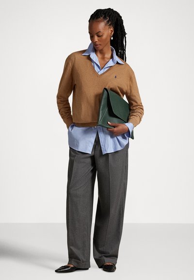 Καφέ μάλλινο πουλόβερ με V λαιμόκοψη πάνω από ανοιχτό γαλάζιο πουκάμισο με κουμπιά, σε συνδυασμό με γκρι παντελόνι φαρδιάς γραμμής και πράσινη δερμάτινη τσάντα χειρός. Φορούνται μαύρα μπαλαρίνες.