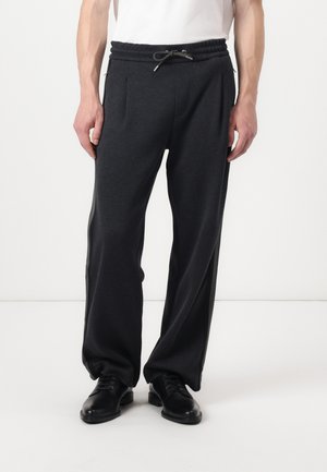 Dark gray sweatpants feature an elastic waistband with a drawstring, side pockets, and a relaxed fit. Paired with black dress shoes.