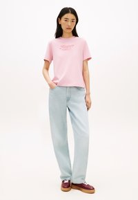 Ροζ βαμβακερό T-shirt με κοντά μανίκια και λογότυπο «Tommy Hilfiger». Συνδυάζεται με ανοιχτό μπλε τζιν ψηλόμεσο και μπορντό αθλητικά παπούτσια.