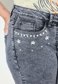 Jeans in denim grigio con applicazioni di perle a forma di fiore e design sparsi sulla tasca posteriore e sulla zona coscia.
