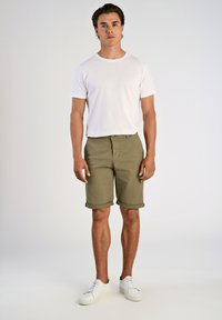 Weißes T-Shirt mit Rundhalsausschnitt kombiniert mit olivgrünen Shorts und weißen Turnschuhen. Die Shorts haben umgeschlagene Säume. Einfaches, lässiges Design.