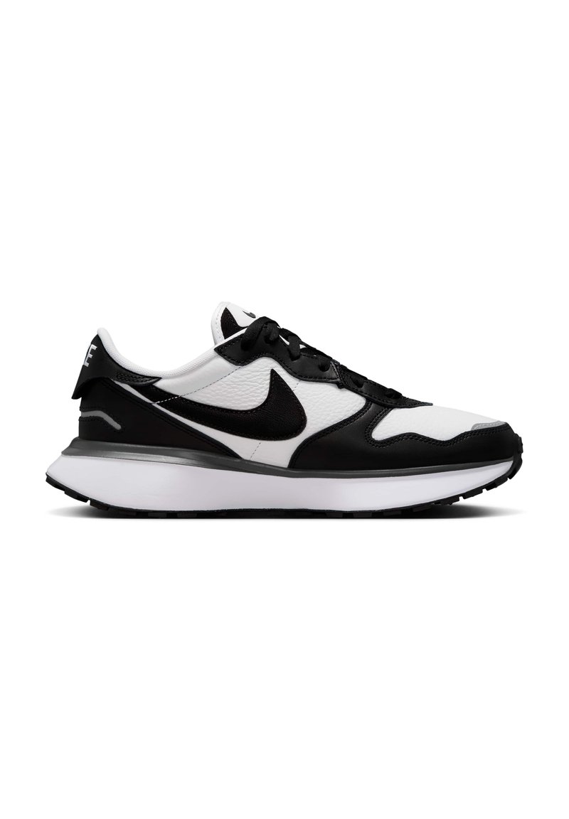 Zapato deportivo en blanco y negro con parte superior de cuero texturizado, puntera redonda, cordones negros y media suela blanca acolchada. Presenta un swoosh negro.