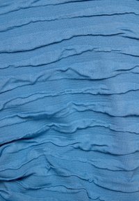 Blauer Stoff mit sich überschneidenden, wellenförmigen Falten. Weiche, strukturierte Oberfläche mit einer einheitlichen Farbe und sanftem Drapierungseffekt.