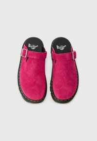Fuchsia suede clogs with a buckle strap, black inner lining, rubber sole, and yellow stitching on the edge.