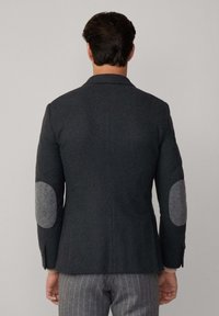 Blazer grigio carbone con una vestibilità sartoriale, dotato di toppe in lana grigia sui gomiti e di una fessura singola sul retro. Realizzato in tessuto testurizzato.