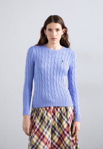 Pull en maille torsadée bleu clair avec un col rond et un ourlet côtelé, associé à une jupe à carreaux multicolore.