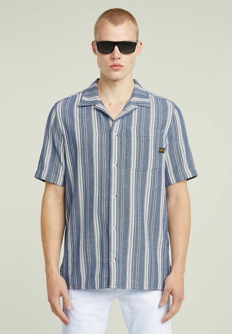 Korte mouwen button-up overhemd in blauw en witte strepen, met een borstzak, zachte stof en casual kraag. Draag met donkere zonnebril.