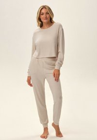 Beżowy zestaw odzieży loungewear z prążkowanej tkaniny, składający się z krótkiego topu z długim rękawem oraz pasujących zwężających się spodni z elastycznymi mankietami i pasem. Miękka tekstura.