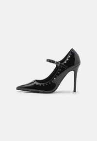 Zwarte lakleren hoge hak schoen met spitse neus, enkelbandje en zilveren studs aan de voorkant. 10 cm hakhoogte.