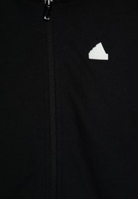 Giacca nera con zip, realizzata in un tessuto texturizzato, dotata di una zip centrale e di un logo Adidas bianco sulla parte sinistra del petto.