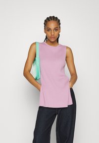 Top de malha canelada rosa claro, sem mangas, com decote redondo, combinado com jeans de perna larga azul escuro e uma mala verde menta.